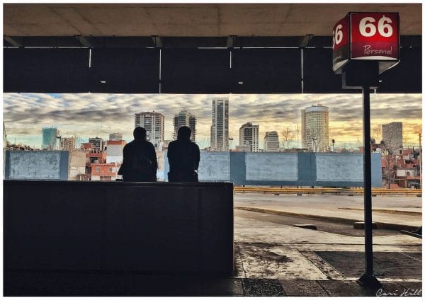 Artistic photo print of a silhouette of two men at Retiro Bus Station in Buenos Aires, Argentina with a dusky cityscape in front of them.